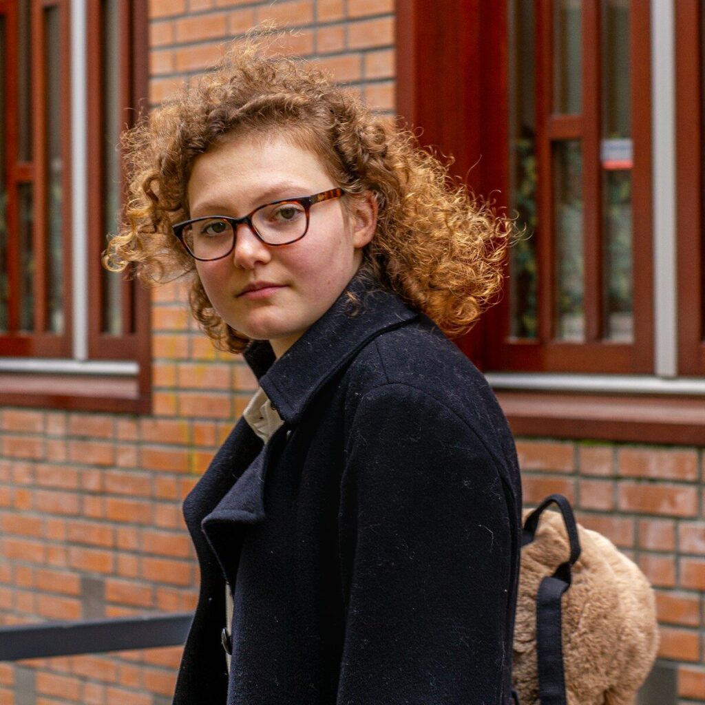 a woman with curly hair and glasses standing in front of a brick building