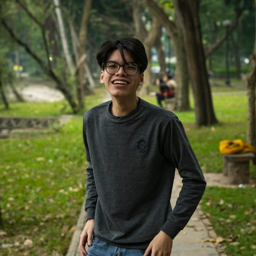 a young man standing in a park with trees in the background